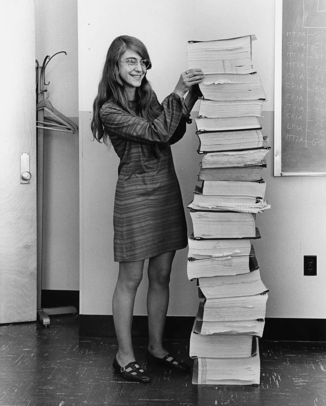 Margaret Hamilton in 1969, smiling beside a stack of printed program listings as tall as she is.